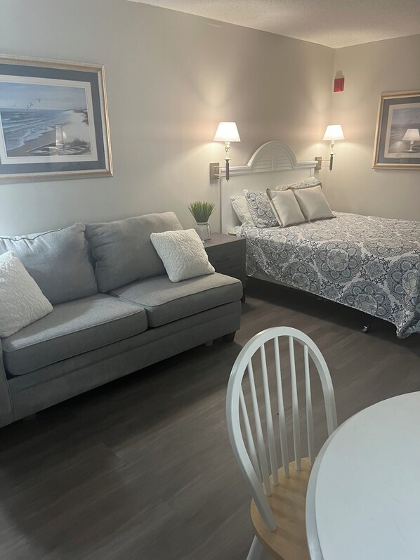 A modern bedroom with a gray sofa, a bed with patterned bedding, two wall-mounted lamps, and framed artwork on the walls.
