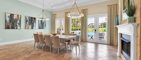 A spacious dining area with a large table and chairs, a fireplace, and artwork on the walls.