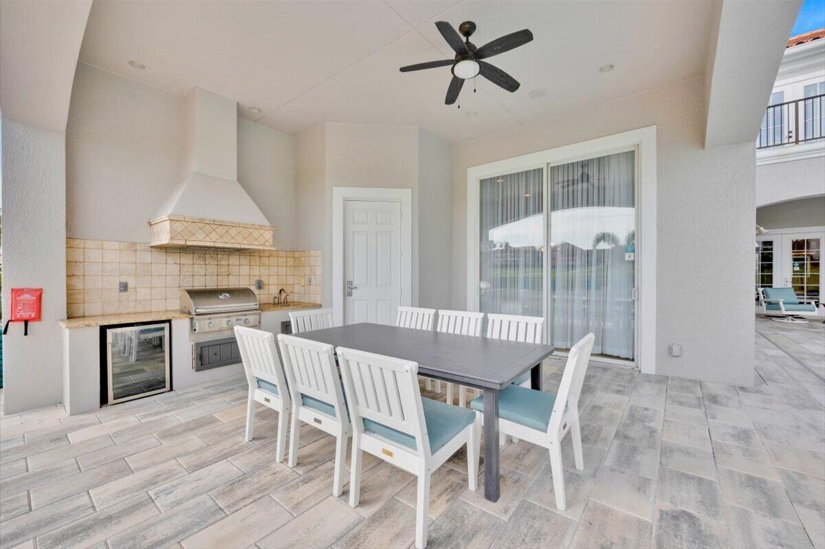 An outdoor patio with a dining table and chairs, a grill, and a ceiling fan.