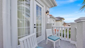 Ein weißer Balkon mit zwei weißen Stühlen und einer Bank, einer weißen Tür und einem weißen Geländer.