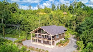 Une cabane à deux étages dotée d’un balcon, entourée d’une forêt dense et bordée d’une route sinueuse.