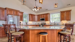 Une cuisine moderne avec des meubles en bois, un réfrigérateur en acier inoxydable, un four à micro-ondes et un grand îlot central doté de tabourets de bar.