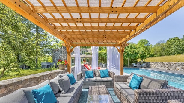 Un espace extérieur aménagé, abrité et doté de meubles en osier, avec vue sur une piscine.