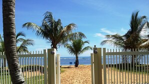 A beach entrance with a gate, palm trees, and a view of the ocean. - Beachfront-Level Private Oasis with Power Backup Generator and A/C for all Areas (Luquillo)
