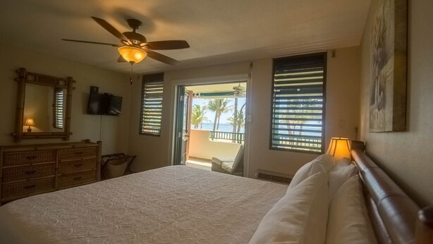 A bedroom with a bed, a ceiling fan, a television, and a view of the beach through the open door. - Beachfront-Level Private Oasis with Power Backup Generator and A/C for all Areas (Luquillo)