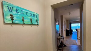 Un couloir orné d’une pancarte « BIENVENUE » représentant des hippocampes, qui mène à une pièce offrant une vue sur l’océan.