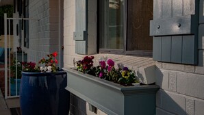 Une maison avec un porche, un grand bac à fleurs et un luminaire fixé au mur.