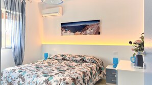 A bedroom with a bed, a bedside table, a wall-mounted air conditioner, a hanging light fixture, and a framed picture on the wall. - GOLDEN SAND - Punta Braccetto  (Punta Braccetto)