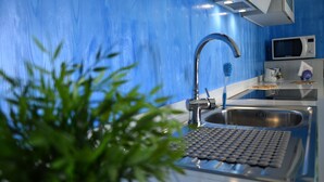 A modern kitchen with a blue backsplash, stainless steel sink, and a microwave. - GOLDEN SAND - Punta Braccetto  (Punta Braccetto)