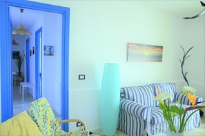 Una sala de estar con sofá, sillón, un cuadro y una planta.