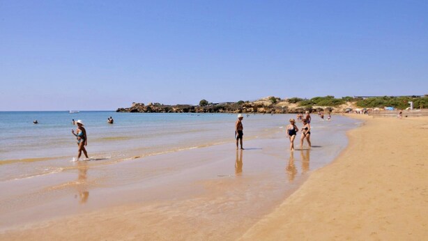 A beach with people walking along the shore, a clear sky, and rocky terrain in the background. - GOLDEN SAND - Punta Braccetto  (Punta Braccetto)