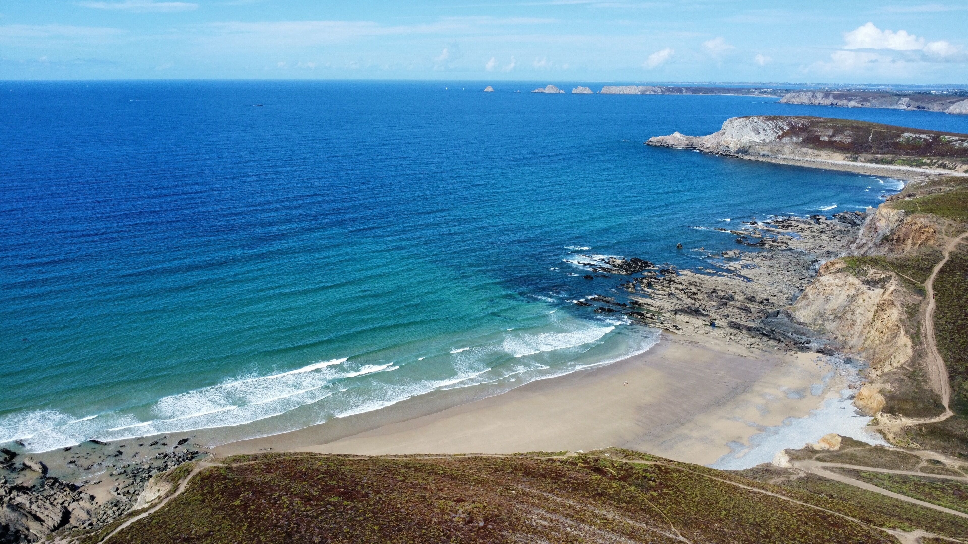 Paesaggio costiero con spiaggia sabbiosa, scogliere rocciose e mare cristallino.