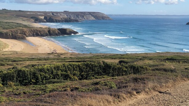Un paysage côtier avec une plage, des falaises et un ciel dégagé.