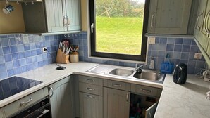 Une cuisine équipée d’un four encastré, d’un évier et d’une fenêtre donnant sur un jardin.