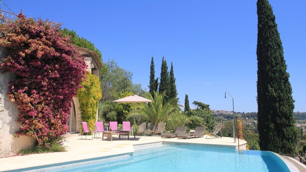 A swimming pool with lounge chairs and a pergola, surrounded by cypress trees and flowering plants. - Contemporary Sea-View Villa with Infinity Pool – Near Saint-Paul de Vence (La Colle-sur-Loup)