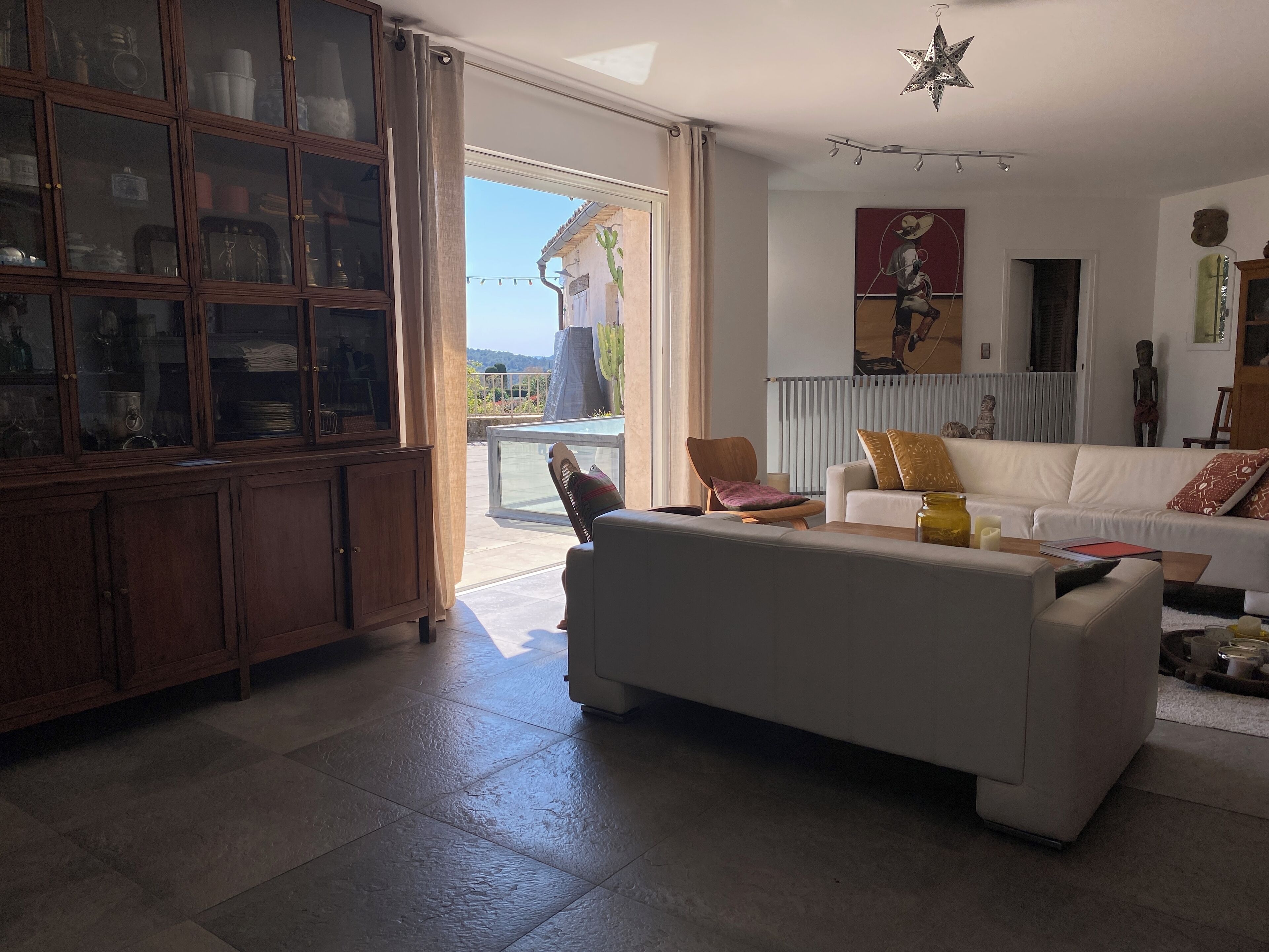 Un salon spacieux avec un canapé blanc, un meuble en bois et une porte vitrée donnant sur un balcon.
