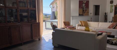 Un salon spacieux avec un canapé blanc, un meuble en bois et une porte vitrée donnant sur un balcon.