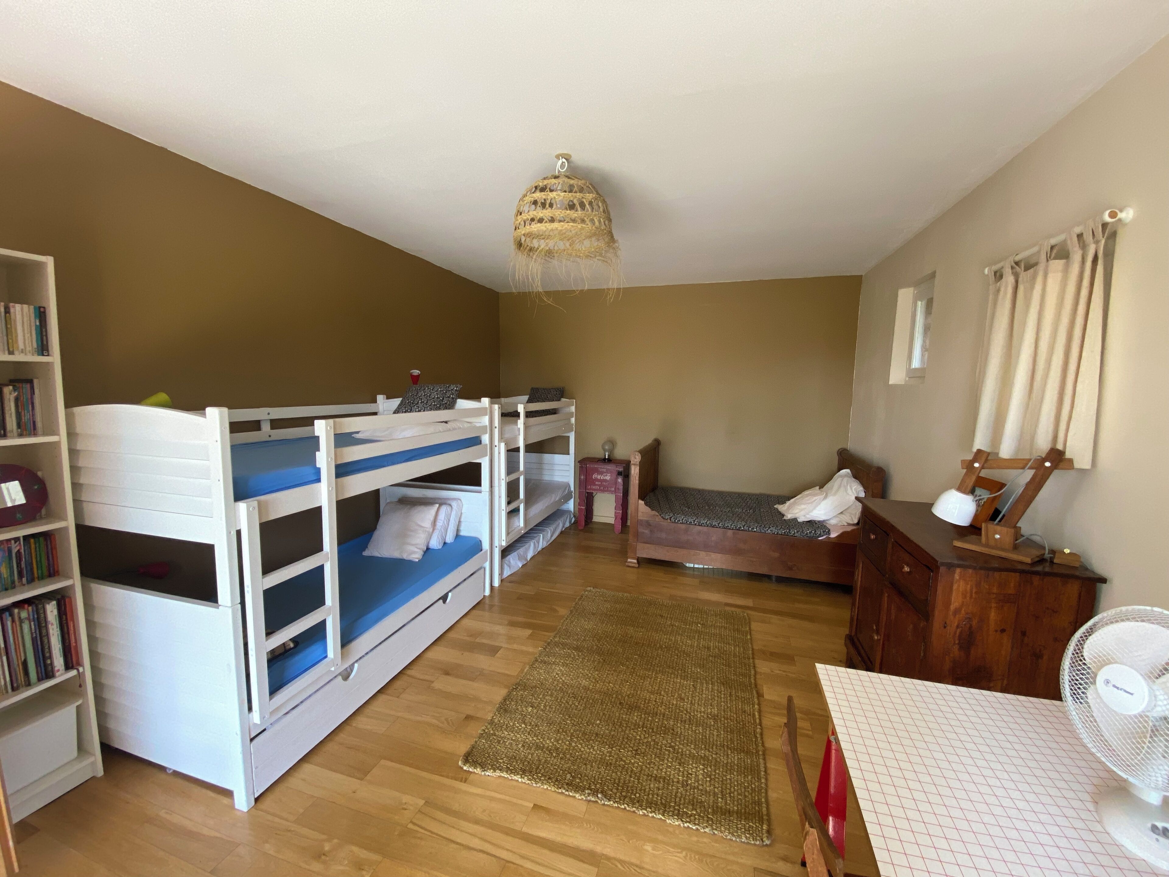 A room with bunk beds, a desk, a chair, a bookshelf, a fan, and a window with curtains.