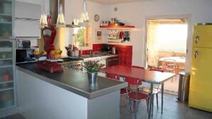 A compact kitchen with a central island, a dining area with red chairs, and a yellow refrigerator. - Contemporary Sea-View Villa with Infinity Pool – Near Saint-Paul de Vence (La Colle-sur-Loup)