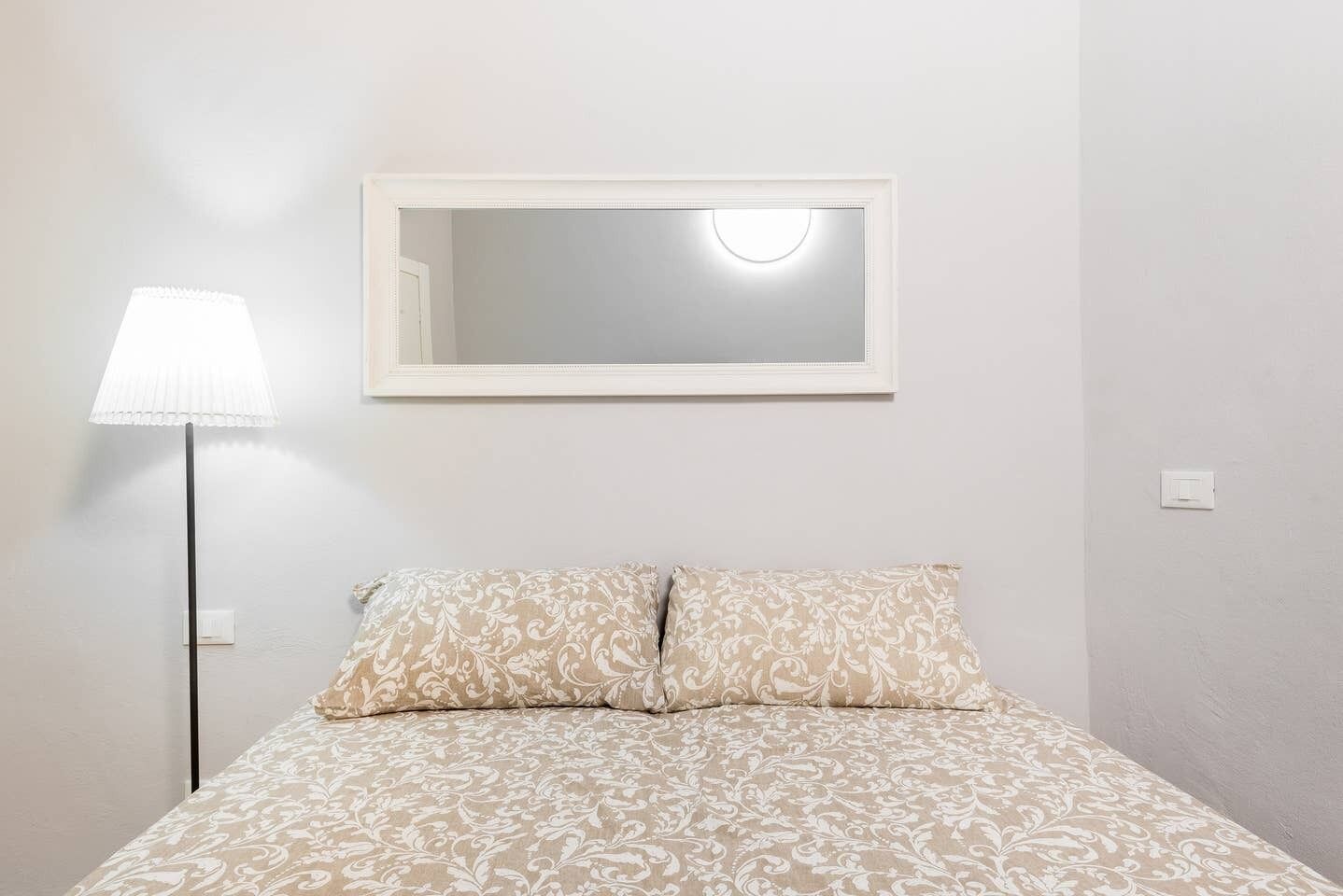 A bedroom with a bed, a bedside lamp, and a mirror on the wall.
