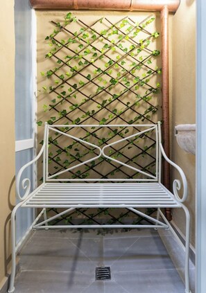 Un banc en métal blanc, adossé à un mur en treillis recouvert de lierre vert.