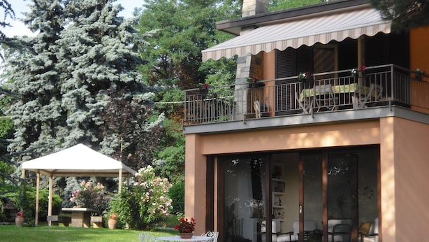 A two-story house with a balcony, a covered patio, and a lawn with a table and chairs.