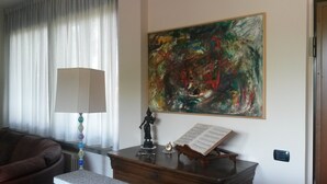 A room with a large abstract painting on the wall, a lamp, a small statue, and a music stand with sheet music.