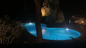 Una piscina de nit amb arbres al voltant i una formació rocosa.