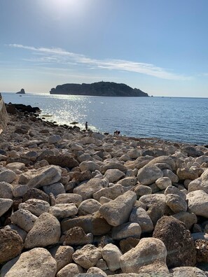 A rocky beach with large boulders and a clear view of the sea and distant landforms.