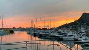 Un port esportiu amb diverses embarcacions amarrades, una superfície d'aigua tranquil·la i un paisatge urbà al fons.