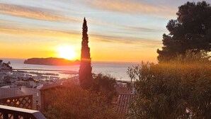 Vista costanera amb un capvespre, un ciri destacat i una escala que condueix a un balcó amb plantes en testos.