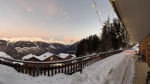 A snow-covered mountain landscape with a wooden chalet and a wooden fence.