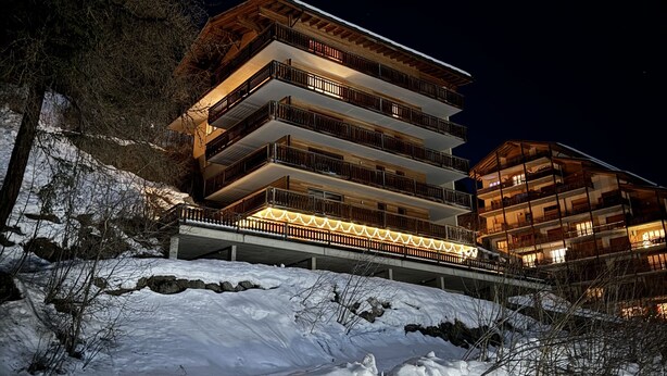 A multi-story hotel with balconies, situated on a snow-covered slope.