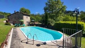 A swimming pool with a stone deck, a stone building, and a well-maintained garden.