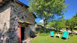 A stone building with a red door, a small garden with grass and potted plants, and two green lounge chairs.