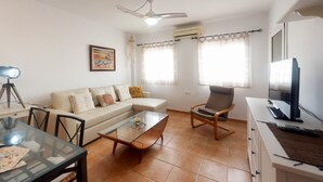 A living room with a sofa, armchair, glass coffee table, and a TV on a stand. - Nice apartment in Cabo de Gata (Cabo De Gata)