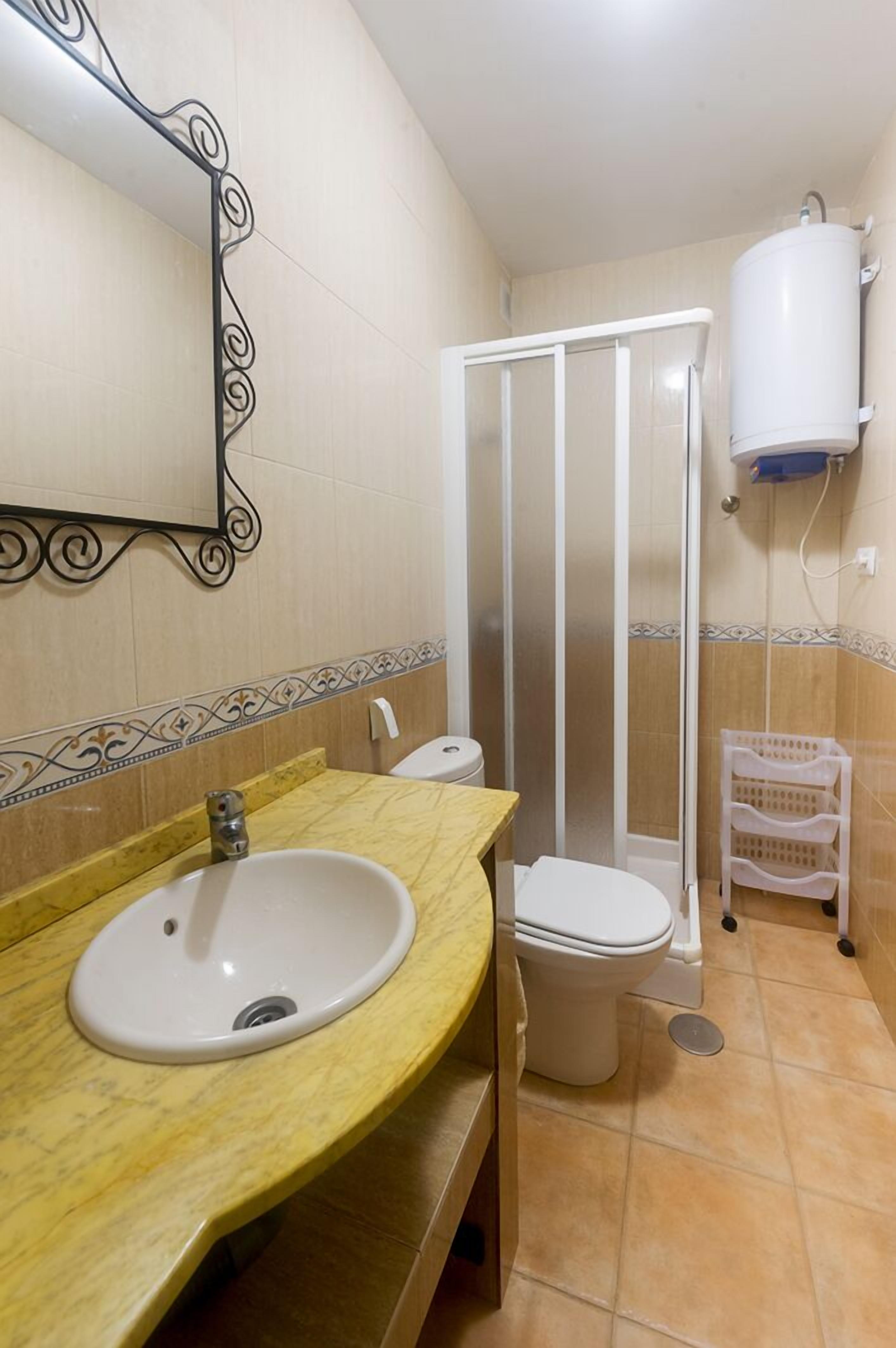 Ein Badezimmer mit Marmorwaschbecken, Toilette, Duschkabine und einem weißen Durchlauferhitzer.