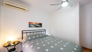 A bedroom with a bed, a nightstand, a wall-mounted air conditioner, a ceiling fan, and a painting on the wall. - Nice apartment in Cabo de Gata (Cabo De Gata)