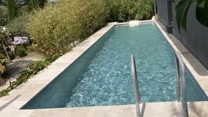 En rektangulär swimmingpool med klart vatten, omgiven av en stenbelagd terrass och frodig grönska.