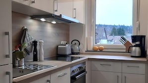 Une cuisine moderne avec des armoires blanches, un four encastré et une fenêtre donnant sur des maisons.
