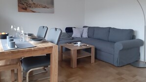 Un salon moderne avec une table à manger en bois, deux chaises, un canapé gris, une table basse et un lampadaire.