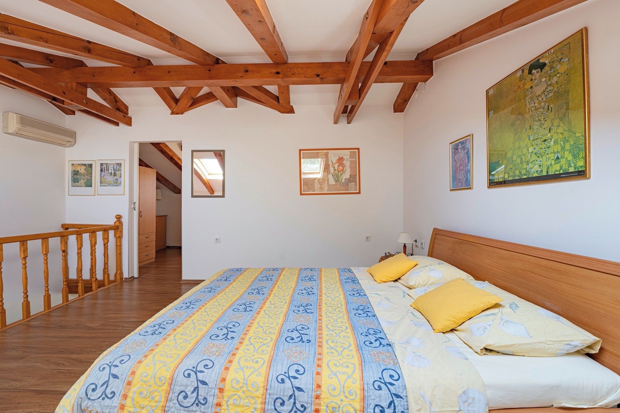 A bedroom with a wooden ceiling, a bed with patterned bedding, and artwork on the walls.