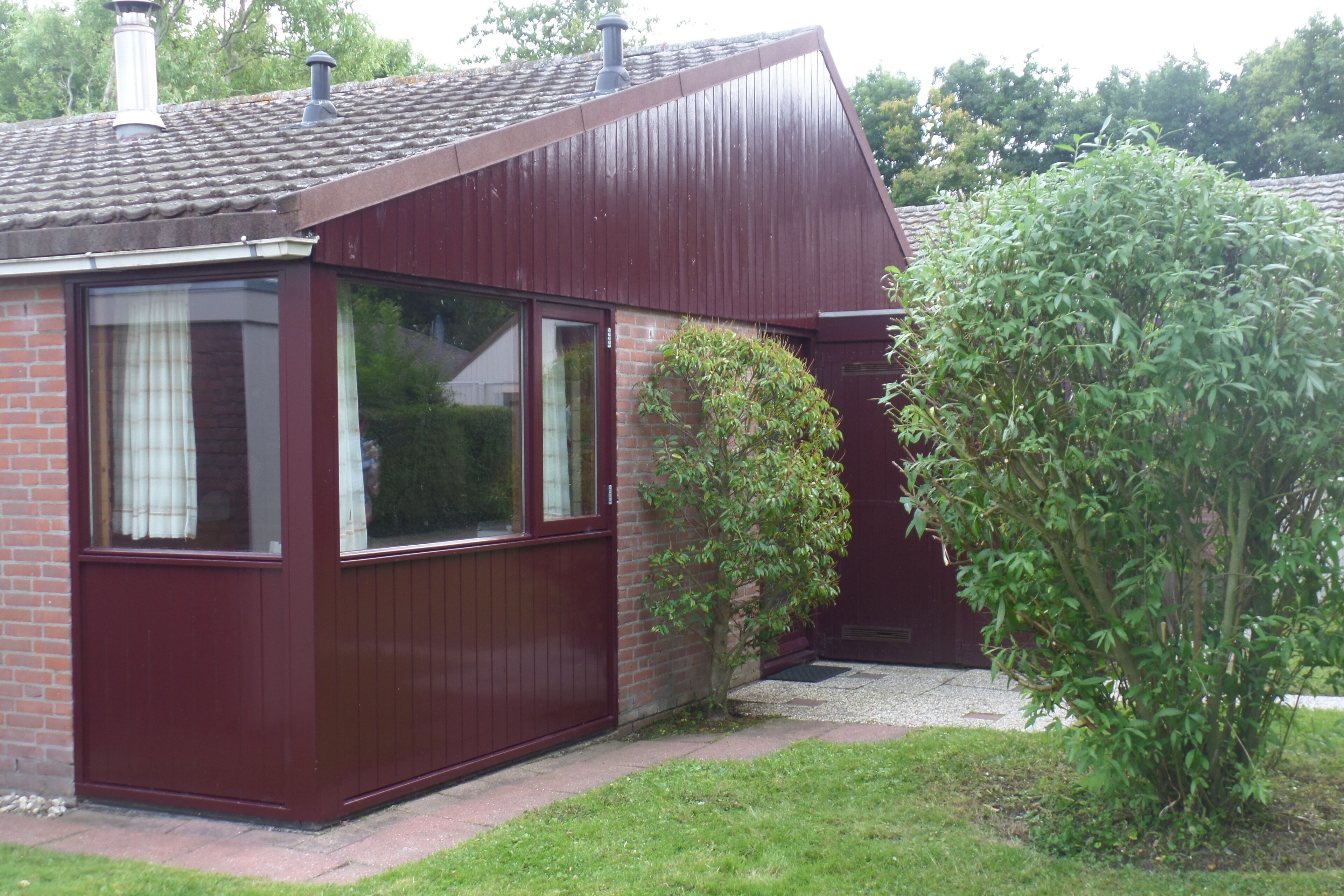 A small, single-story house with a red exterior and a brick foundation.