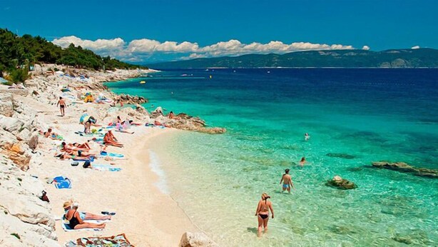 A beach with clear turquoise water, people sunbathing, and rocky terrain.