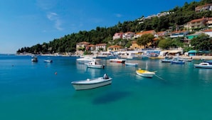 A coastal town with boats docked along the shore, buildings on a hillside, and a clear blue sea.