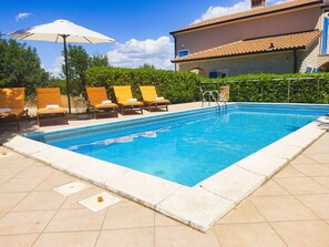 A swimming pool with lounge chairs and umbrellas, surrounded by a hedge and a building with a tiled roof. - Luxury villa with pool in a small Istrian village near the sea (Labin)