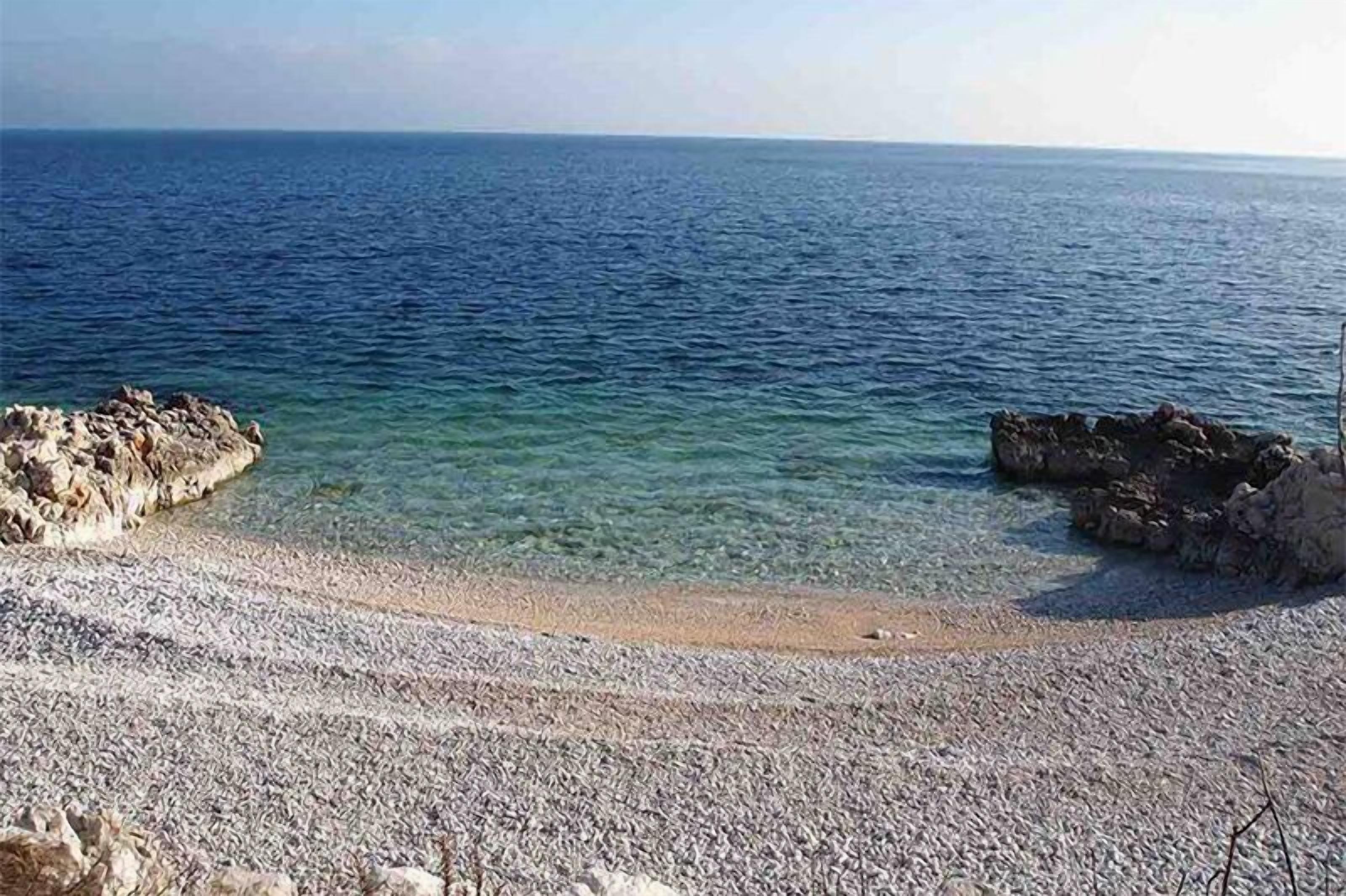 A pebble beach with clear water and rocky outcrops.