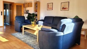 A living room with a wooden ceiling, two blue sofas, a coffee table, and a bookshelf. - big holiday house with grassland in the Vulkaneifel, near Nürburgring and Maare (Lissendorf)