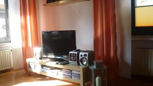 A living room with a television, speakers, and a shelf with decorative items. - big holiday house with grassland in the Vulkaneifel, near Nürburgring and Maare (Lissendorf)