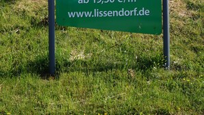 A welcome sign for Lissendorf with a website URL and construction cost per square meter. - big holiday house with grassland in the Vulkaneifel, near Nürburgring and Maare (Lissendorf)